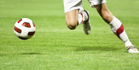 芝生の上でサッカーボールと選手の足が写っている写真。選手はボールを蹴ろうとしている。